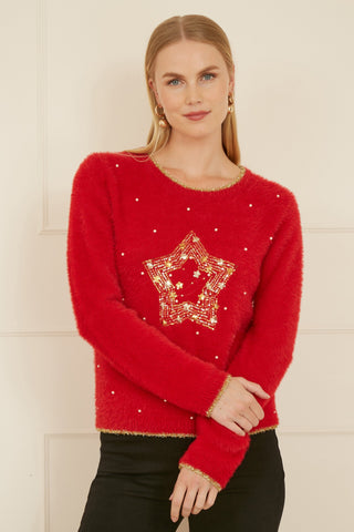 Woman wearing red knitted fluffy Christmas star jumper with gold embellishments and black pants