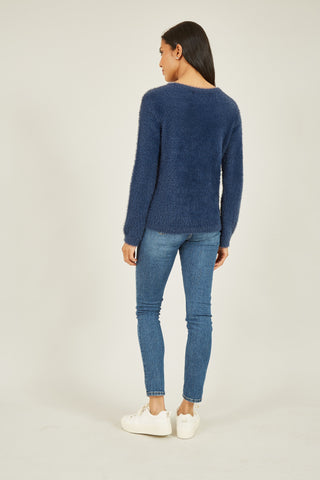 Woman wearing navy sequin snowflake fluffy jumper with blue jeans and white sneakers, back view