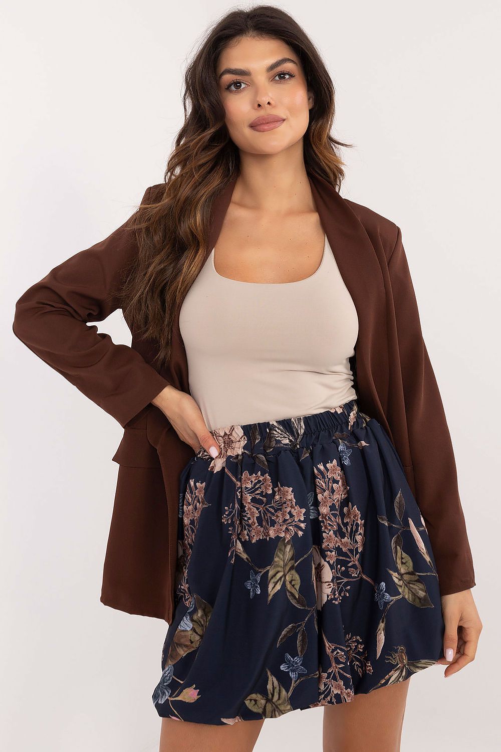 Woman wearing floral patterned mini skirt in bomber style paired with beige top and brown blazer