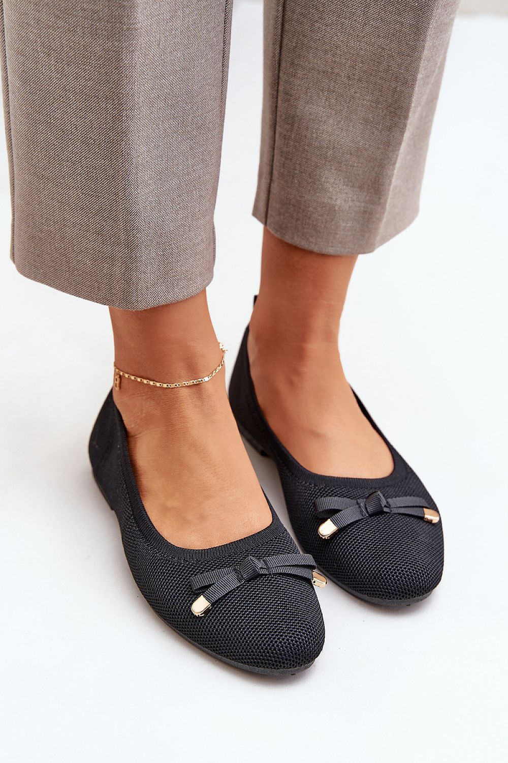 Women's black mesh ballet flats with a bow, eco-leather insole, styled with grey trousers.