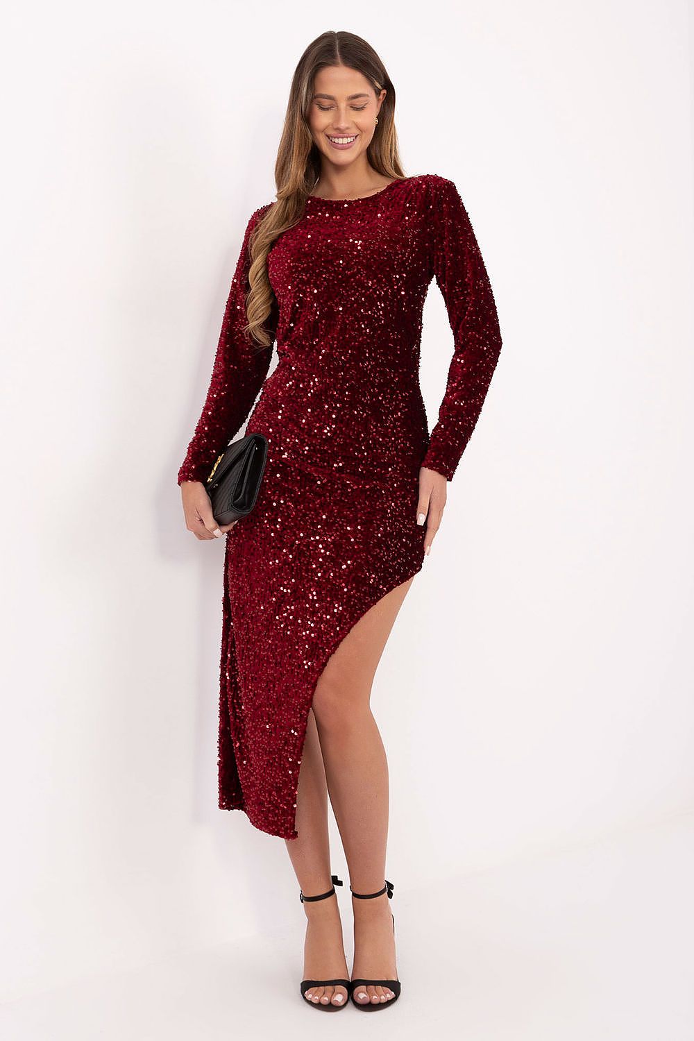 Woman wearing a red evening sequin dress with asymmetrical hem and long sleeves, holding a black clutch and wearing black heels.