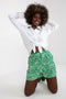 Damen Shorts with green patterned design, elastic waistband, and side pockets, styled with a white tied blouse.