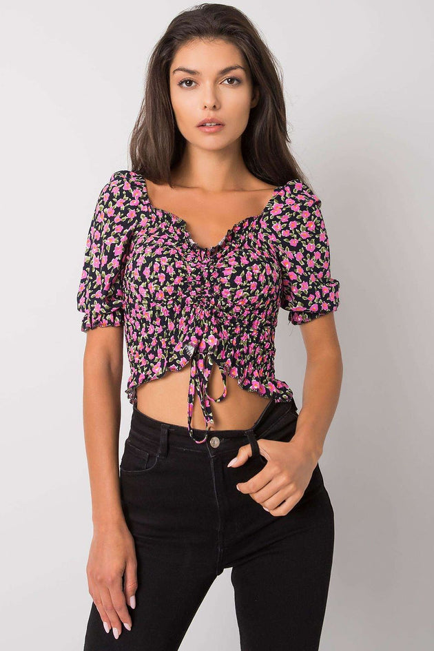 Black women's cropped blouse with colorful floral pattern, V-neck, ruched front with tie, short sleeves, and elastic waistband.