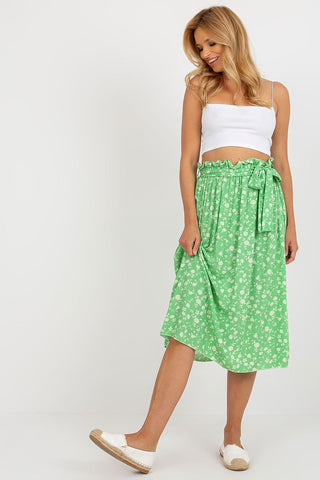 Green midi skirt with white floral pattern and tie belt worn by woman in white crop top and white slip-on shoes